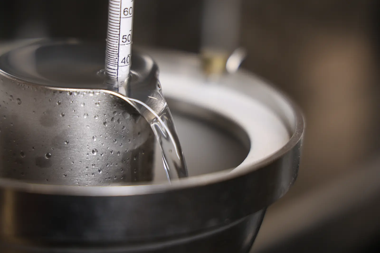 Clear distillate running through a stainless-steel funnel with a thermometer